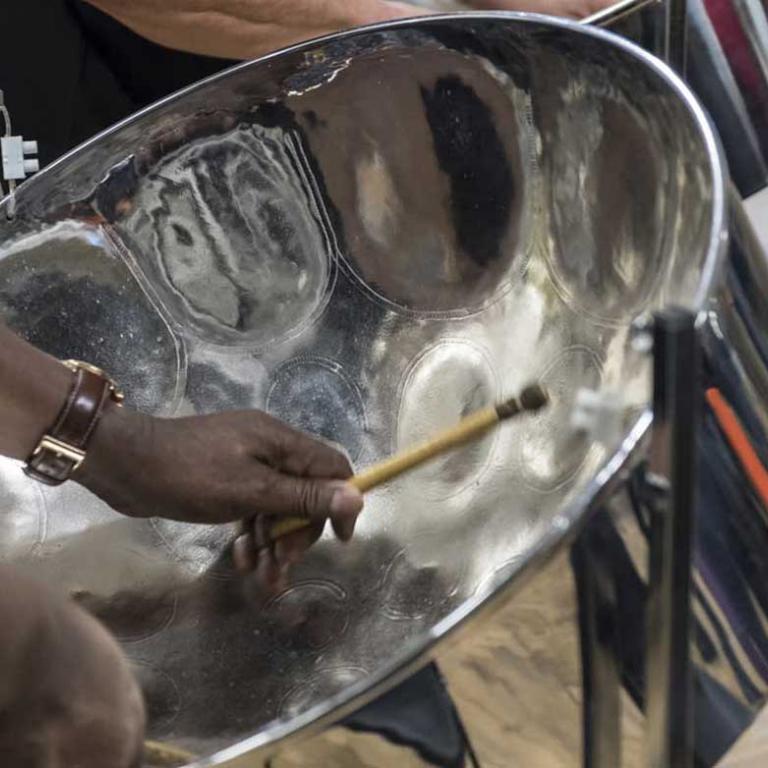 This is a close-up photo of a member of the Glissando Steel Band. The photo focuses on the inside of the steel drum with the players hands in shot