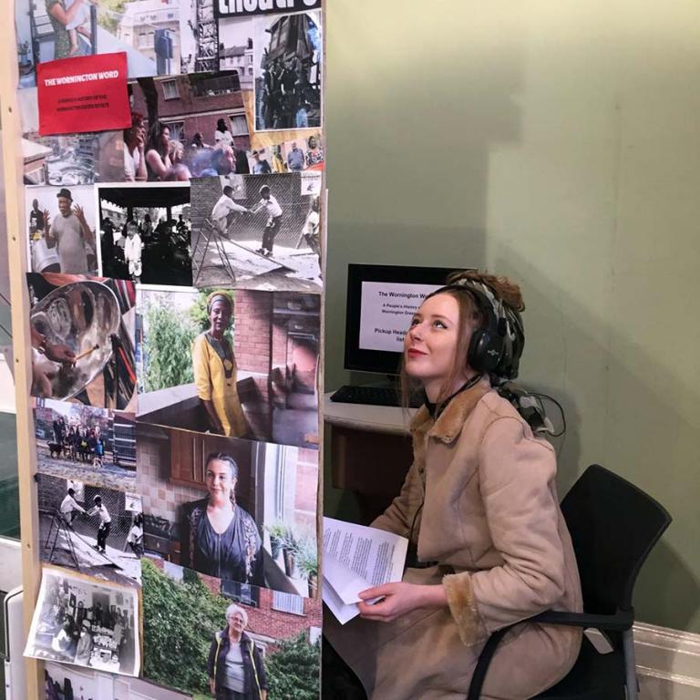 Wornington Green resident Alessana Hall looking and listening to The Oral History Booth set up inside North Kensington Library. The booth was set up so people could interact with the recorded histories of Wornington Green Estate residents whilst seeing their photographs taken of the estate. Photo taken by Natasha Langridge 2019.