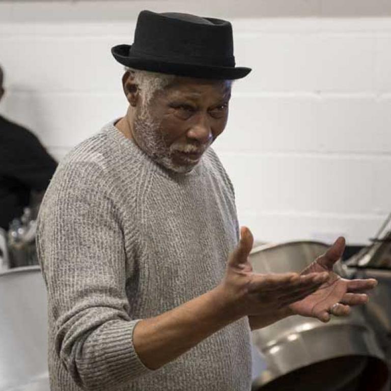 Photo depicts Leslie Palmer, MBE a Notting Hill Carnival Pioneer in the foreground talking to the residents and locals all of which are attending the Wornington Word launch at the venture Centre. In the background are steel drums, two members of the Glissando Steel Band and Ladbrooke Grove legend, Adam Ritchie
