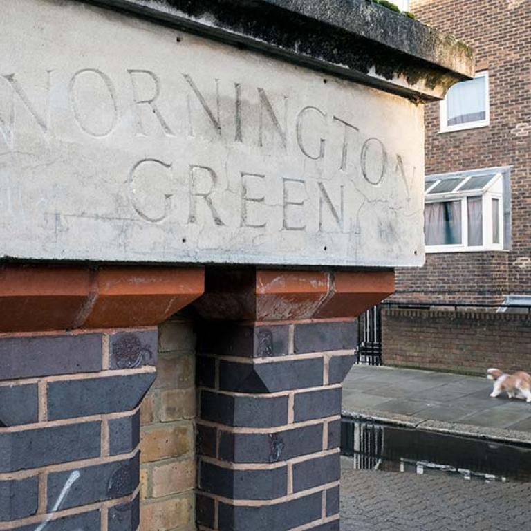 The estate name is inscribed on a white facade mounted on a stand-alone brick feature that is situated on Wornington Road. A local walks their King Charles Cavalier dog in the background. Photo by Kevin Percival.