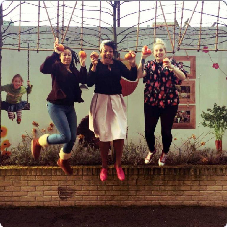 Photo captures three members of Venture Centre staff who are in mid-flight after jumping from a wall outside the Centre. The women are laughing and holding fruit and vegetables in their hands to promote healthy eating. From left to right: Michelle Poponne, Naami Padi and Jessica McMillian. Photo reproduced from @VentureCentre1 Twitter feed, 2016.