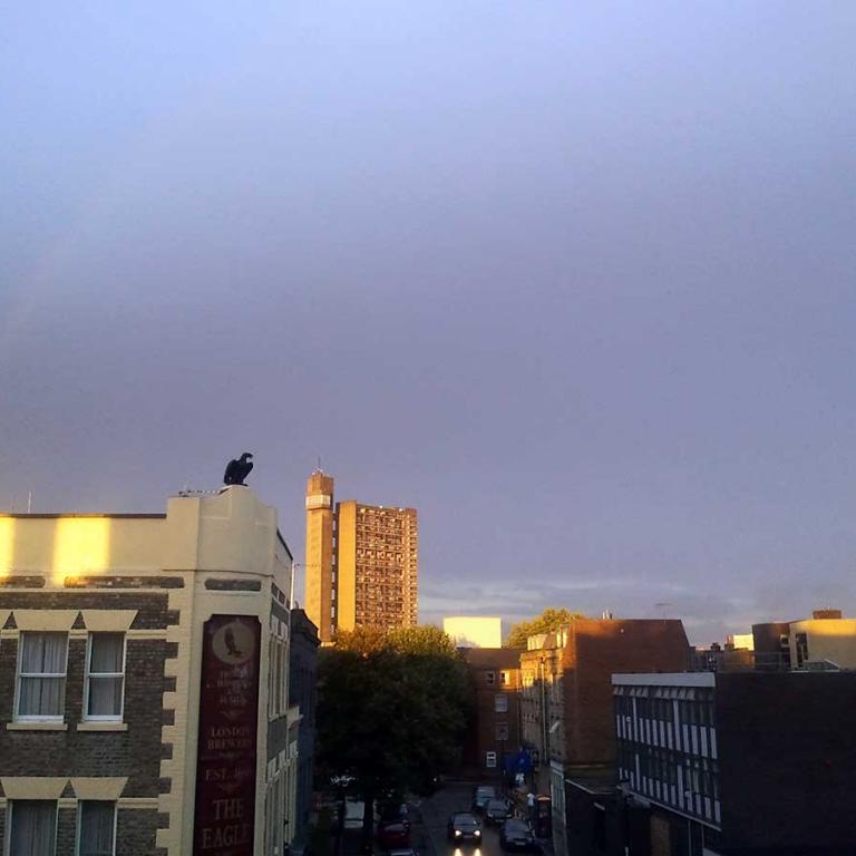 Photo depicts a rainbow over a brass eagle statue that sits on top of the Victorian built Eagle pub on the junction of Ladbroke Grove and Telford Road. In the background Trellick Tower is bathed in golden sunlight. To the bottom right is the Lloyd Williamson prep school. The trees of Wornington Green and Wheatstone House are seen between the pub and the school. Photo taken by Junior Tomlin, 2014.