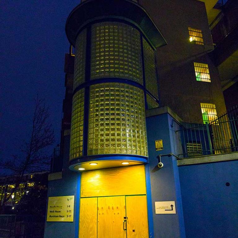 The boarded up main entrance to Rendle, Wells and Murchison Houses on Portobello Road at night time. The entrance has a curved glass facade that was added onto the original brick entrance in the 1990s. Photo by Patrick Gorman, 2018.