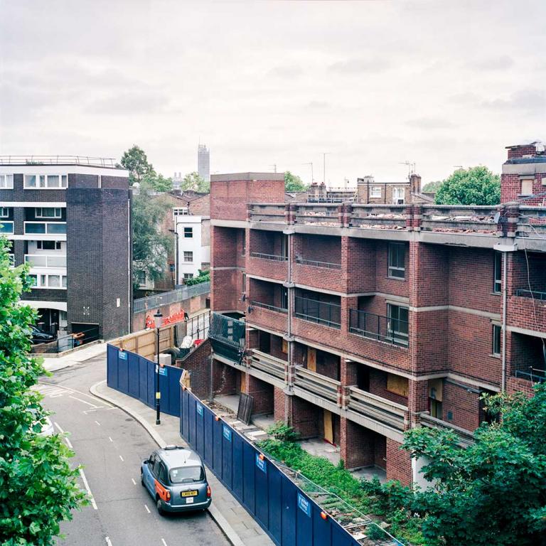 View South-west from the 4th floor of Macaulay House towards Murchison House, during the first stages of demolition. Trees line Portobello Road which runs in front of Murchison House, which is fenced off from the rest of the estate. A taxi is parked on the road, outside the enclosure. Photo by Kevin Percival, a resident of Pepler House, 2019.